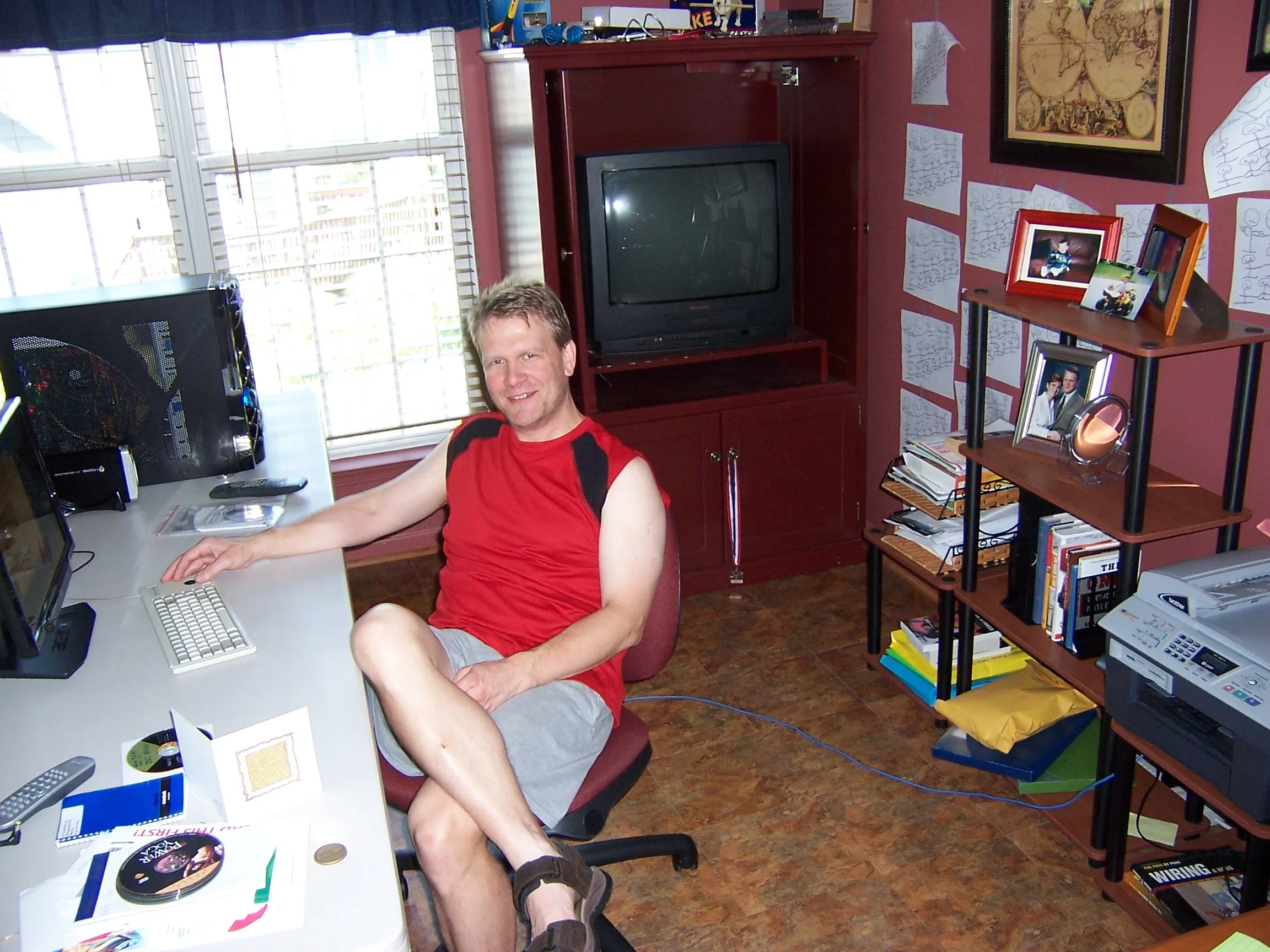 Mid-2000s Bill kicked back in a red tank top at a white desk, a boxy CRT looming in the red cabinet behind him and a cream Brother laser MFC holding down the shelf