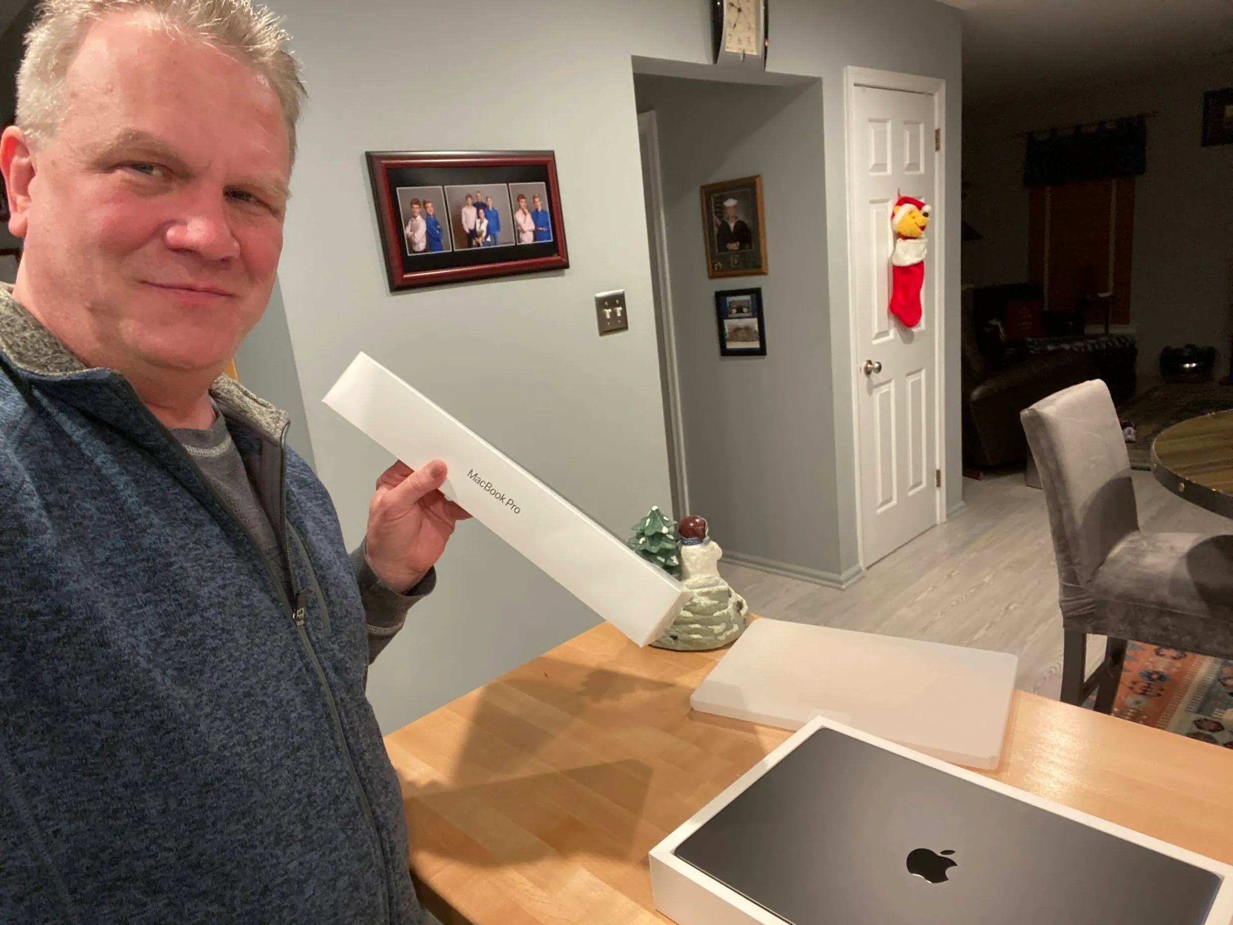 Bill grinning at the kitchen counter as he slides a brand-new MacBook Pro out of its box like treasure